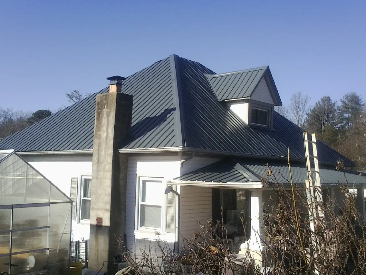 Dark blue standing seam metal roof on a white farmhouse with dormer — Slate & Tile Roof Repair by Roofing Brothers in Placitas