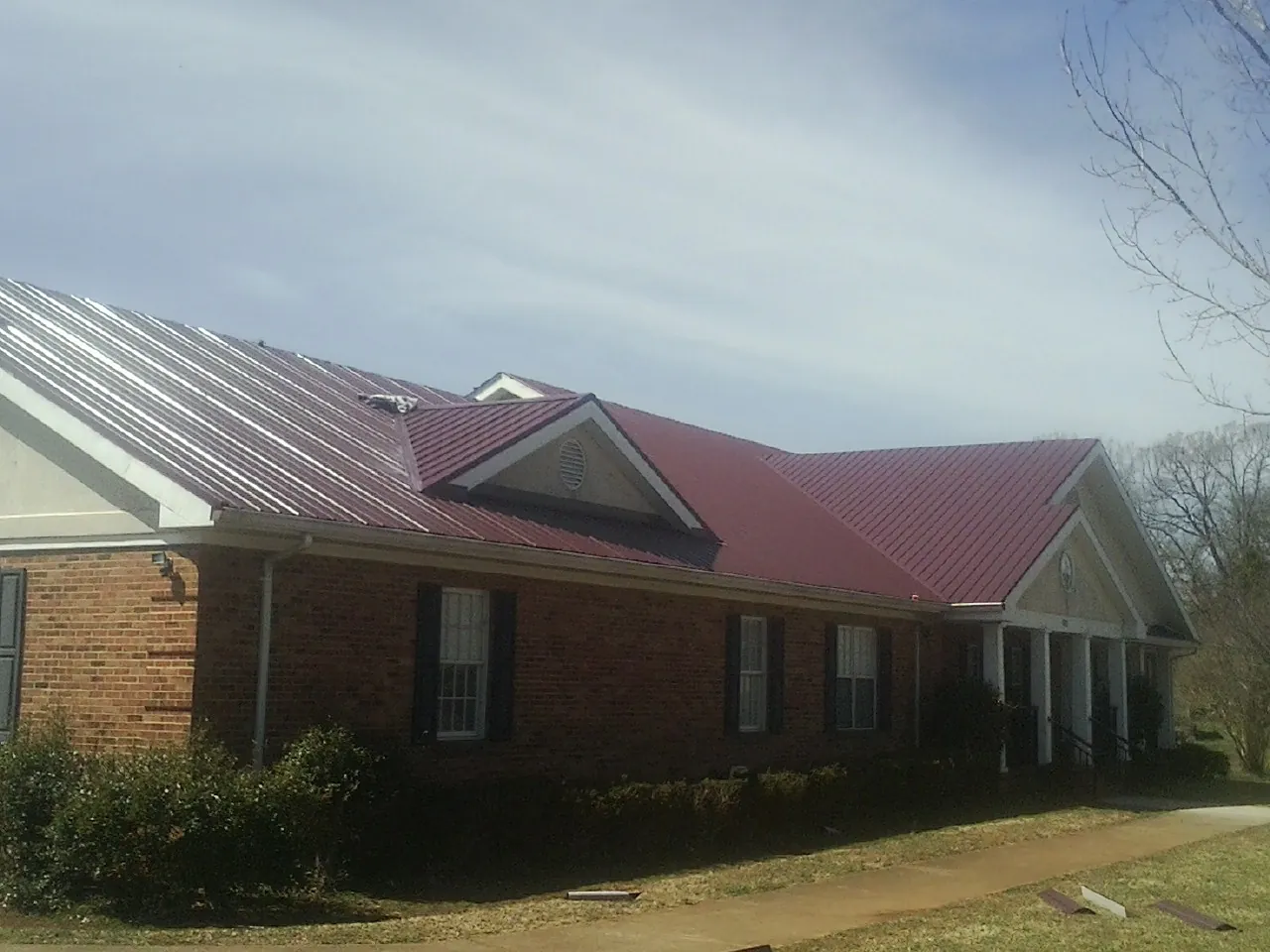 Red metal roof with gabled entries on a long brick building, from a Hail Damage Roof Repair job in Placitas