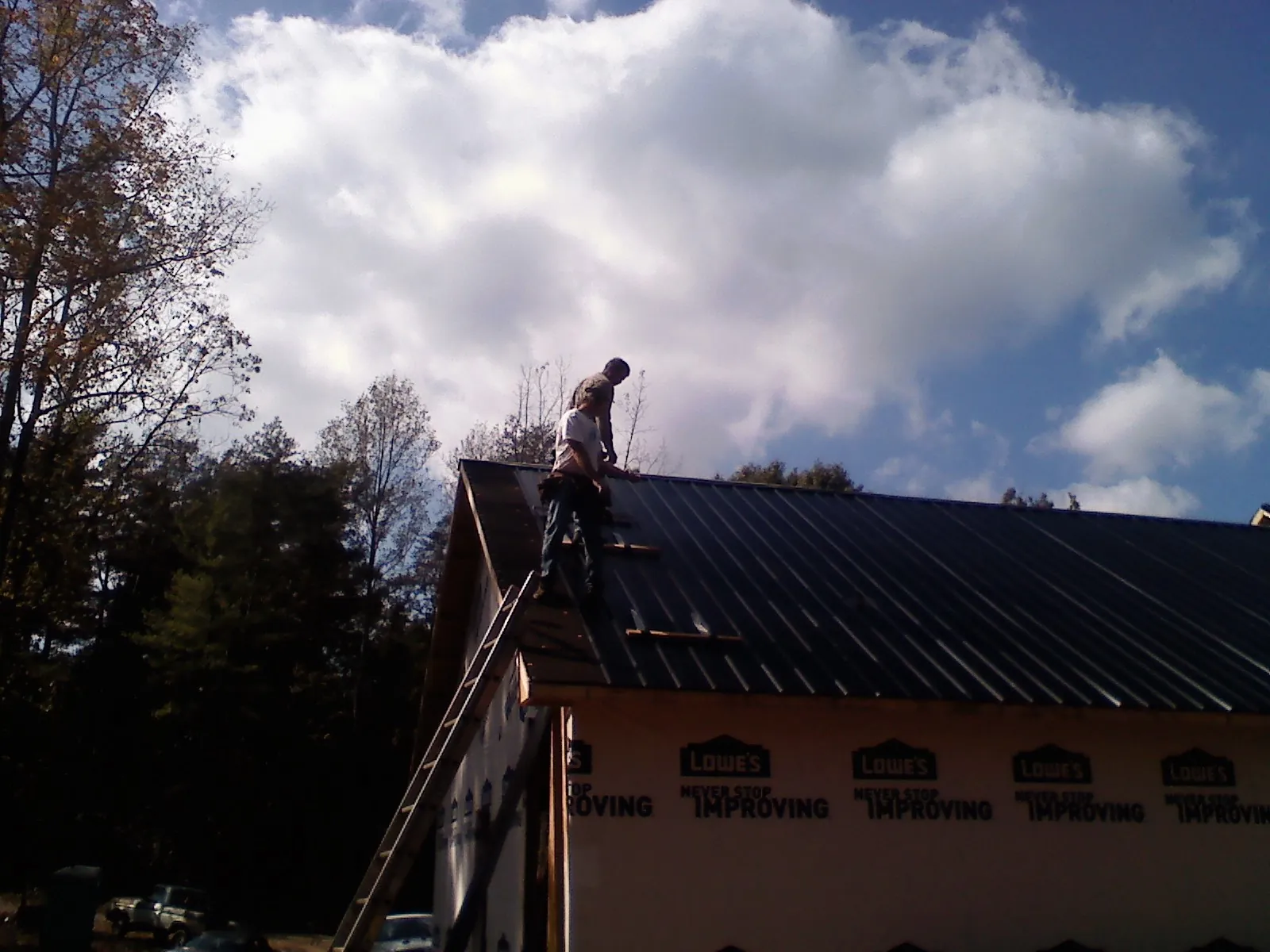 Roofer fastening dark metal panels high against a cloudy sky, from a Roof Inspection job in Placitas