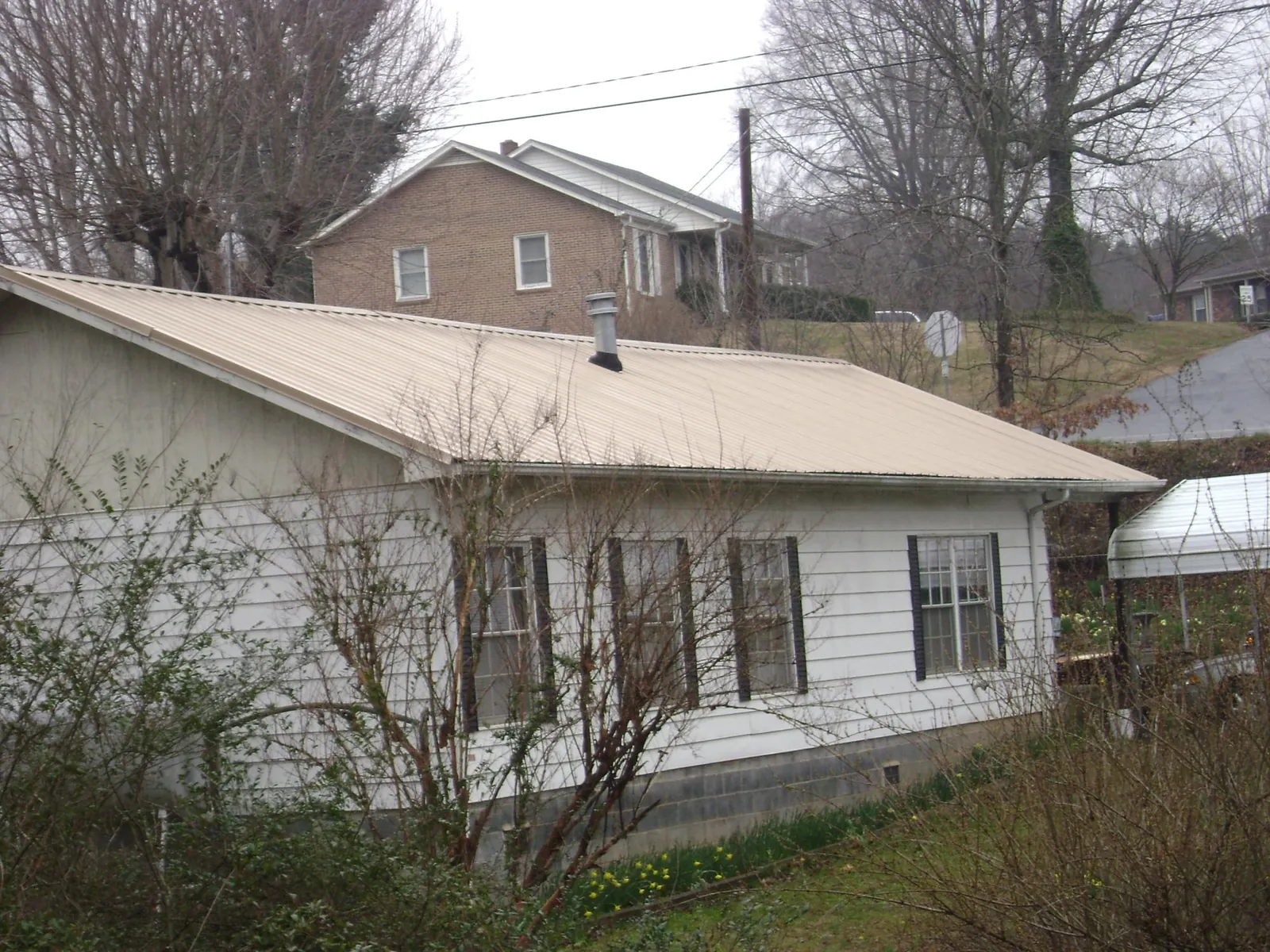 Tan metal roof on a white sided house set into a hillside — Commercial Roofing by Roofing Brothers in Placitas