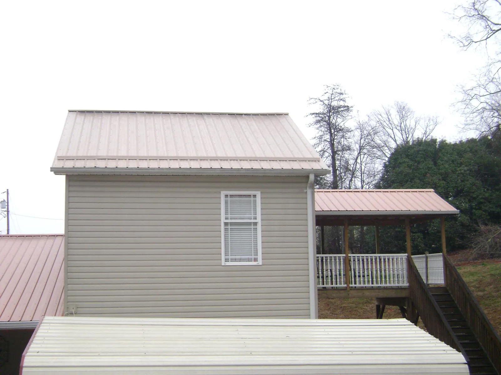 Tan metal roofs on a two story addition and attached porch, from a Roof Replacement job in Placitas